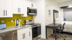 A compact kitchen with white cabinets, a microwave, an oven, and a toaster. - Peachtree Suites (Jersey City)