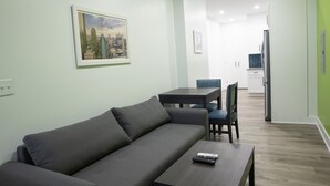 A modern living room with a grey sofa, a coffee table, and a dining area with a table and chairs. - Peachtree Suites (Jersey City)