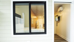 A hotel room with a large window, a bed, a wardrobe, and a television mounted on the wall. - Peachtree Suites (Jersey City)