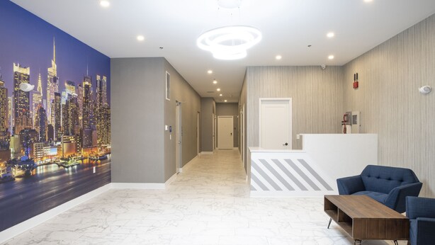 A hotel lobby with a cityscape mural, a reception desk, and seating area. - Peachtree Suites (Jersey City)