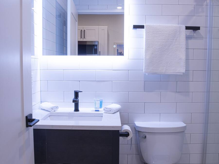 Ein modernes Badezimmer mit Waschbecken, Spiegel und Toilette in Weiß. Handtücher und eine Dusche sind sichtbar.