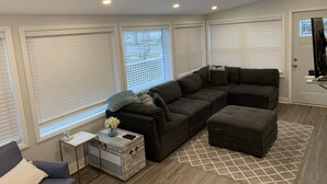 Una sala de estar moderna con un sofá modular, una mesita auxiliar y un ventanal con persianas.