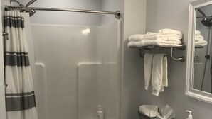 Un baño moderno con ducha de vidrio, inodoro, lavabo con encimera de mármol y toallero con toallas dobladas.