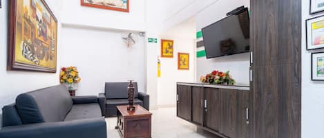 A modern lobby with a sofa, a small wooden table, a TV on a cabinet, and framed artwork on the walls.