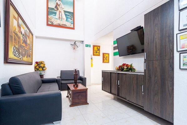 A modern lobby with a sofa, a small wooden table, a TV on a cabinet, and framed artwork on the walls. - Hotel Union (Valledupar)