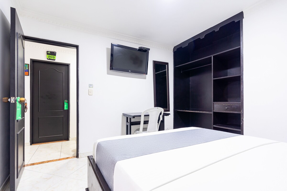 A hotel room with a bed, a desk, a chair, a TV, and a wardrobe.