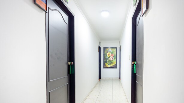A hallway with doors on both sides, a tiled floor, and a painting on the wall. - Hotel Union (Valledupar)