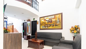 A lobby with a reception desk, a grey sofa, a wooden coffee table, and a painting on the wall. - Hotel Union (Valledupar)