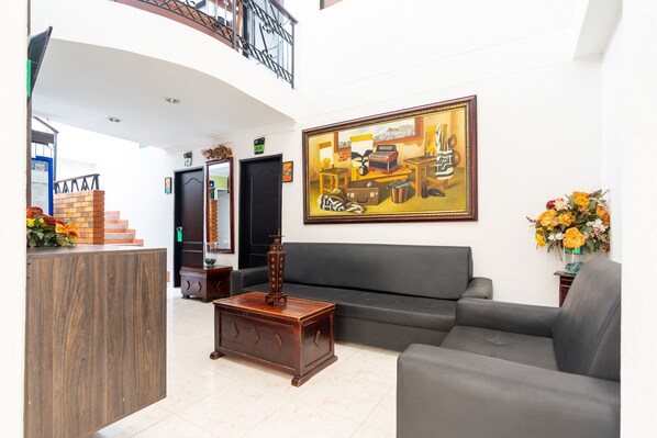 A lobby with a reception desk, a grey sofa, a wooden coffee table, and a painting on the wall.