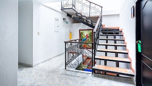 A staircase with a black metal railing, a painting on the wall, and a door with a green sign. - Hotel Union (Valledupar)