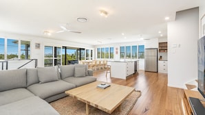 A modern living room with a grey sectional sofa, a wooden coffee table, and a dining area with wooden chairs.