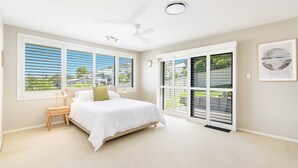 A bedroom with a bed, a nightstand, a ceiling fan, and large windows with blinds.