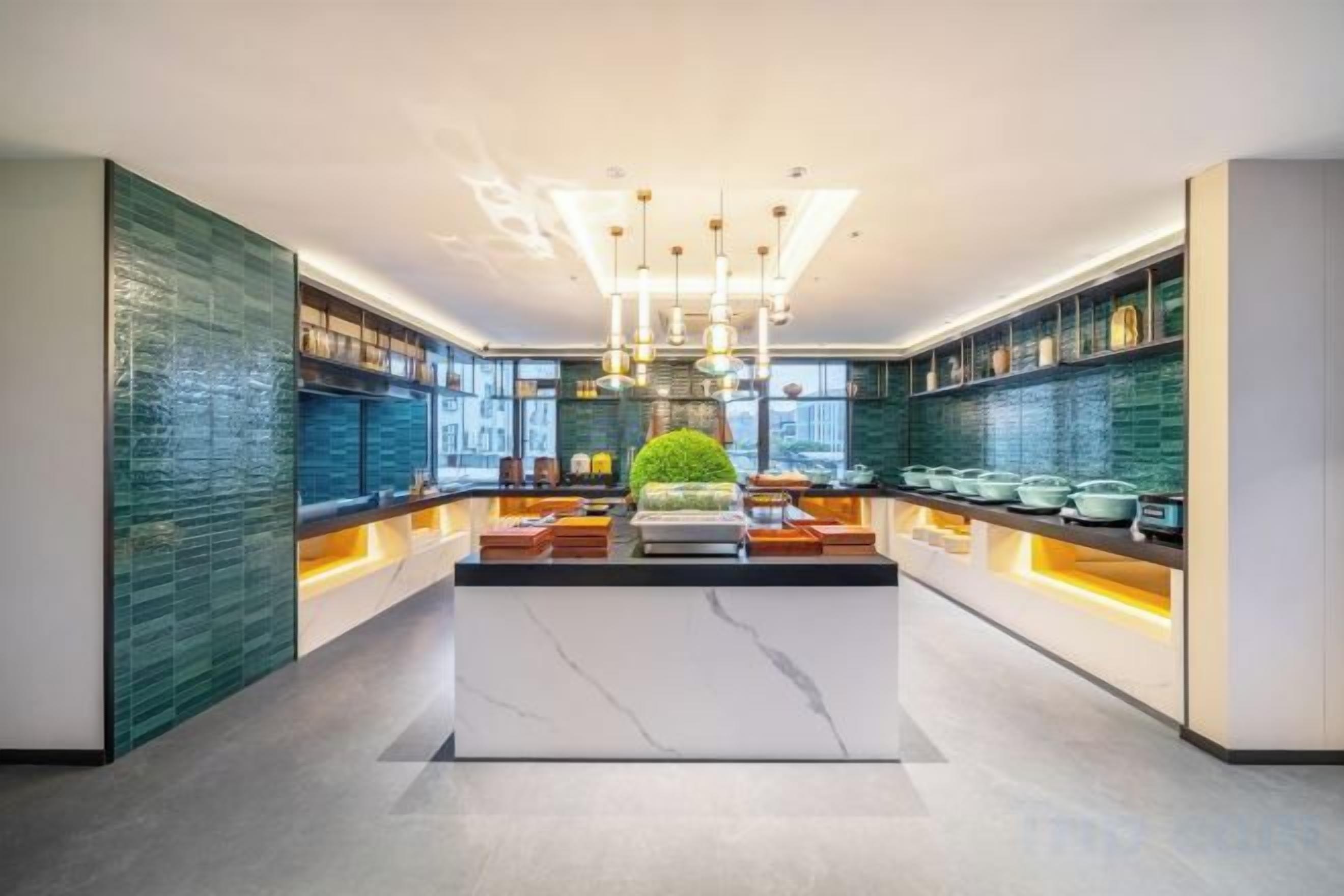 A modern kitchen with a central island, pendant lighting, and a green plant.