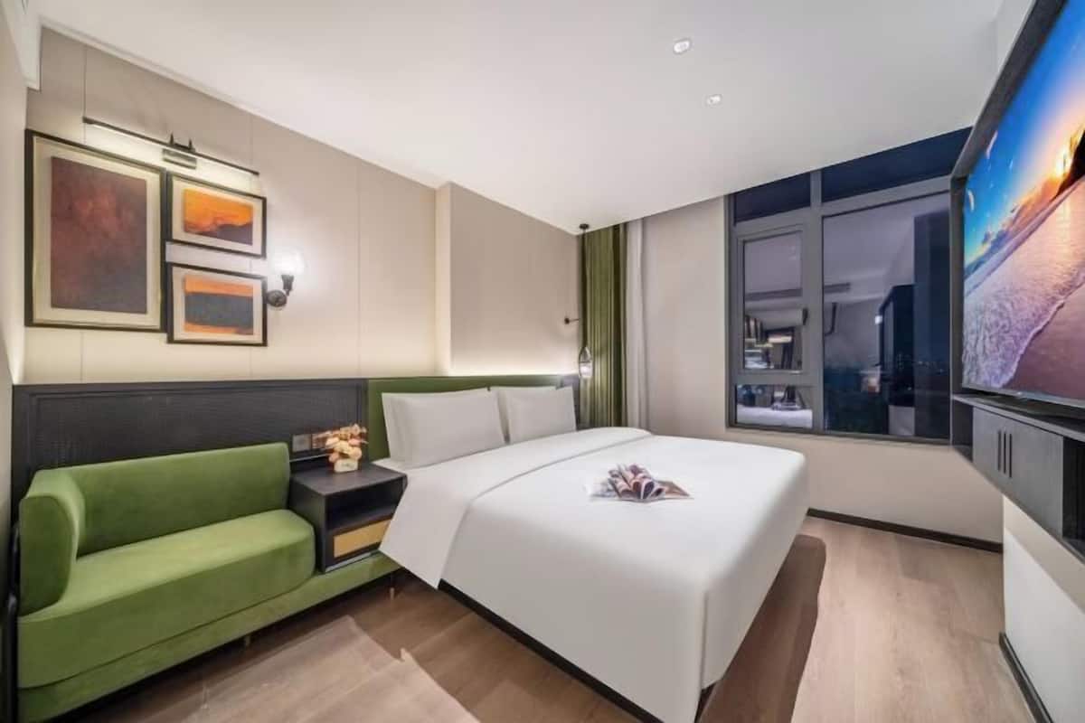 Une chambre d’hôtel avec un lit, un canapé vert, une table de chevet et une grande fenêtre.