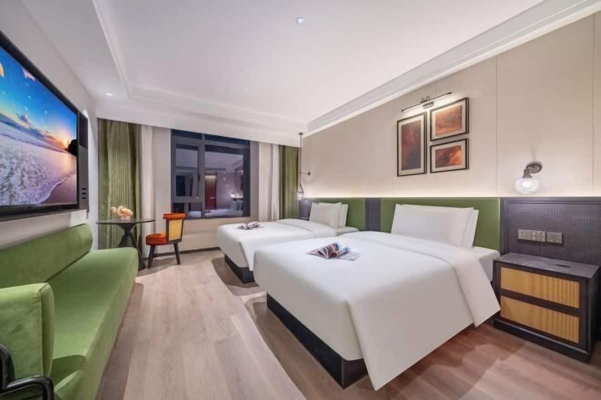 Une chambre d’hôtel avec deux lits, un canapé vert, une télévision, un bureau et une fenêtre.
