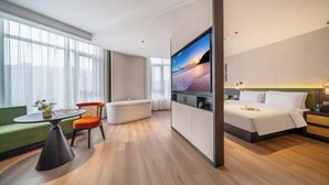 Et moderne hotelværelse med seng, siddeområde med bord og stole, stort tv og udsigt til byen.