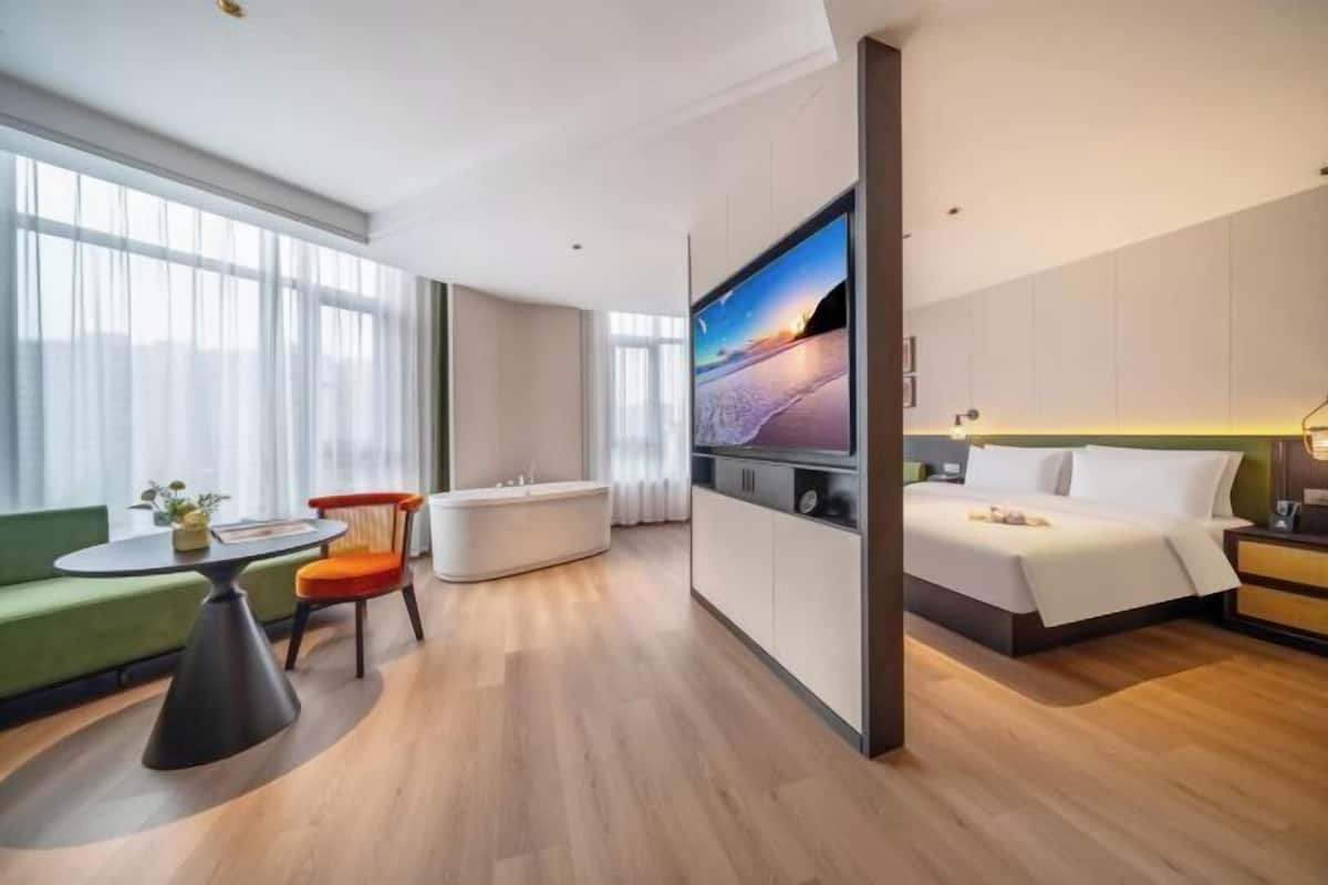 Une chambre d’hôtel moderne équipée d’un lit, d’un coin salon avec une table et des chaises, d’une grande télévision et offrant une vue sur la ville.