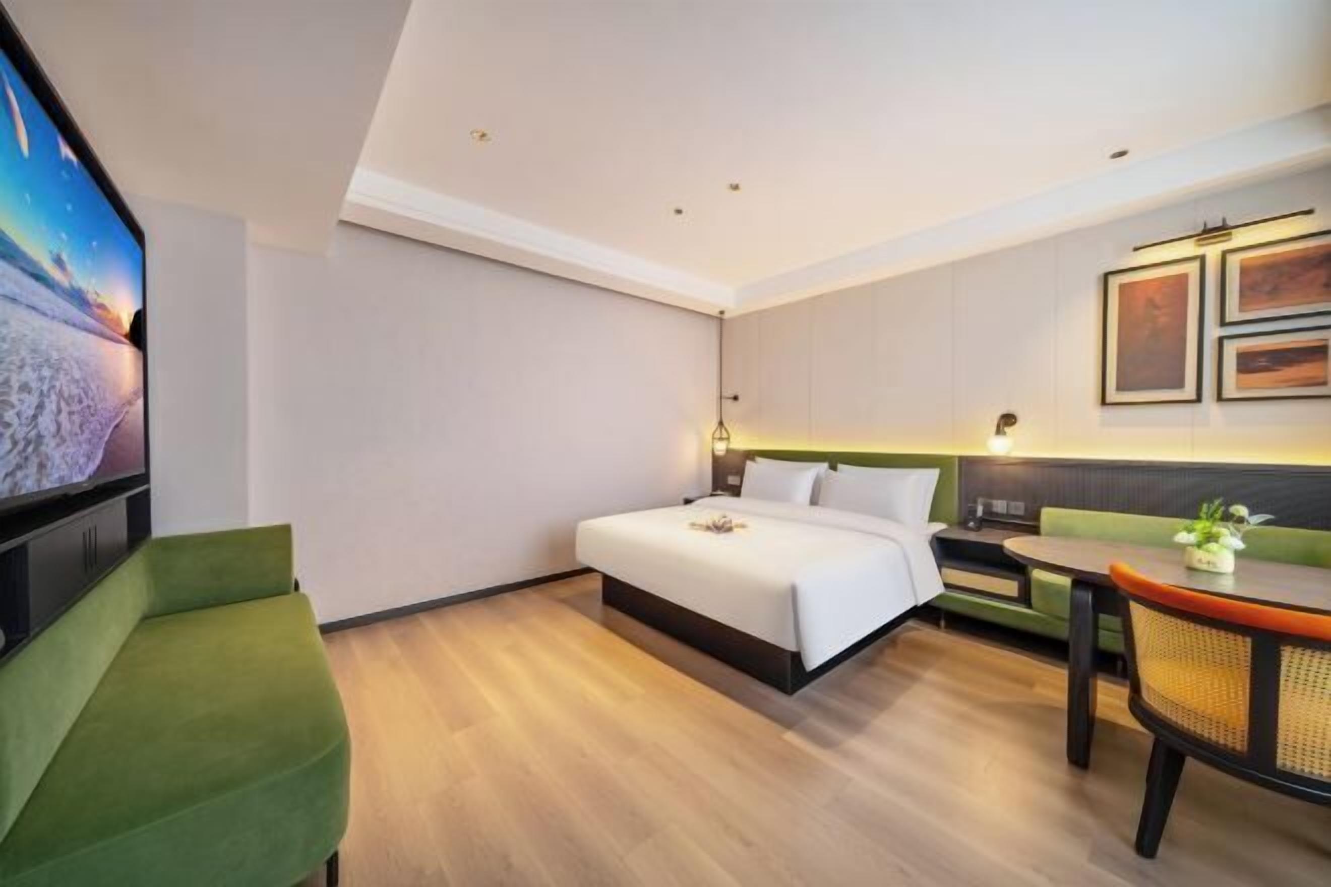 A hotel room with a bed, a green chair, a dining table, and a TV.