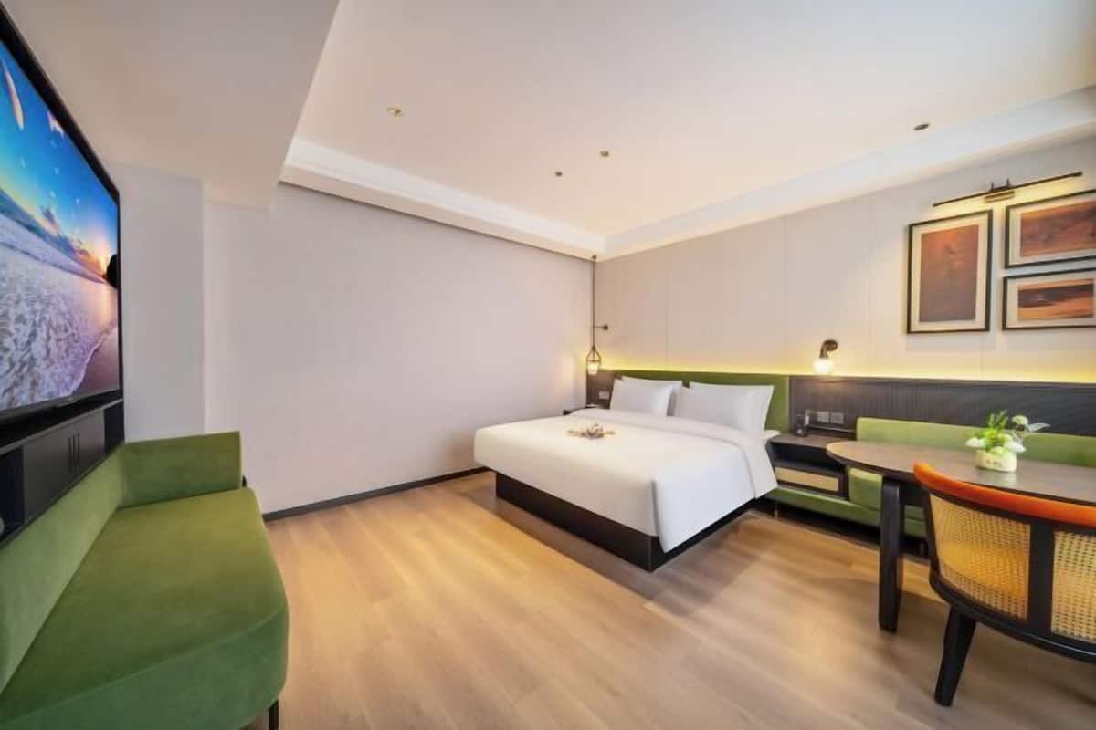 Une chambre d’hôtel avec un lit, un fauteuil vert, une table à manger et un téléviseur.