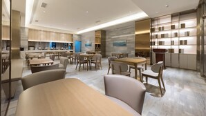 Un espace de restauration moderne avec plusieurs tables et chaises, une cuisine en arrière-plan et une bibliothèque remplie de livres.