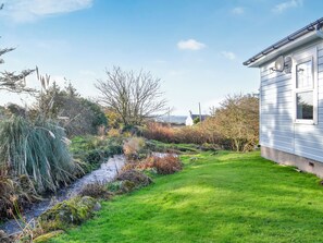 A house with a grassy yard and a small stream. - A superb 4 bedroomed cottage with glorious gardens and stunning sea views. (Newton Stewart)