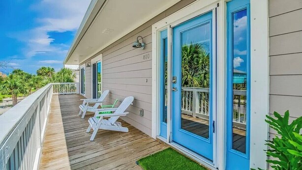 A wooden deck with white chairs, a blue door, and a number 810 sign. - Pissitaway Getaway (Pensacola Beach)