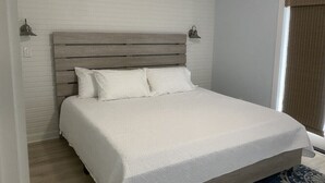 A bedroom with a wooden headboard, white bedding, and a patterned rug. - Pissitaway Getaway (Pensacola Beach)