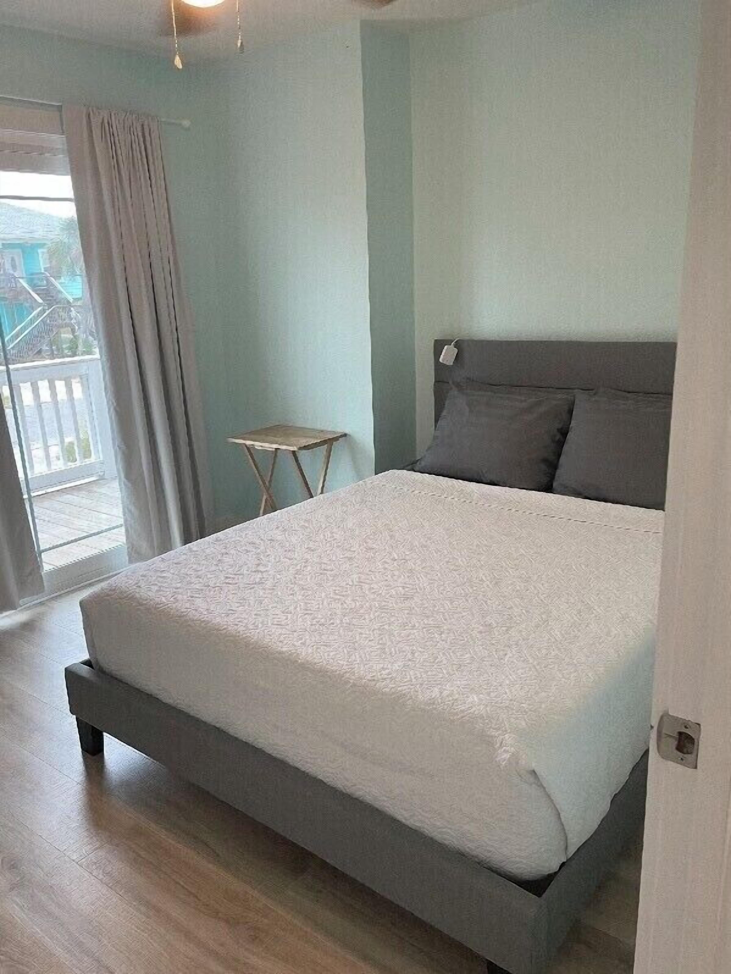 A bedroom with a bed, a small table, and a view of the outdoors.