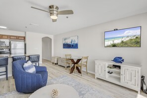 A modern living room with a dining area, a ceiling fan, a flat-screen TV, and a kitchen in the background. - Windancer 304. Gulf Front, Free Beach Service, Heated Pool, Sugar Sand, Grill (Miramar Beach)