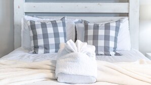 A neatly made bed with a folded white towel in the center, a checkered pillow, and a white headboard. - Atlantic View Heated Pool/Spa/Firepit/Beach/Golf/Sleeps 12 (St. Augustine)