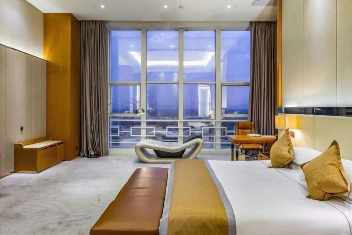 Habitación de hotel con una cama grande, un escritorio, una silla y vistas a través de un ventanal amplio.