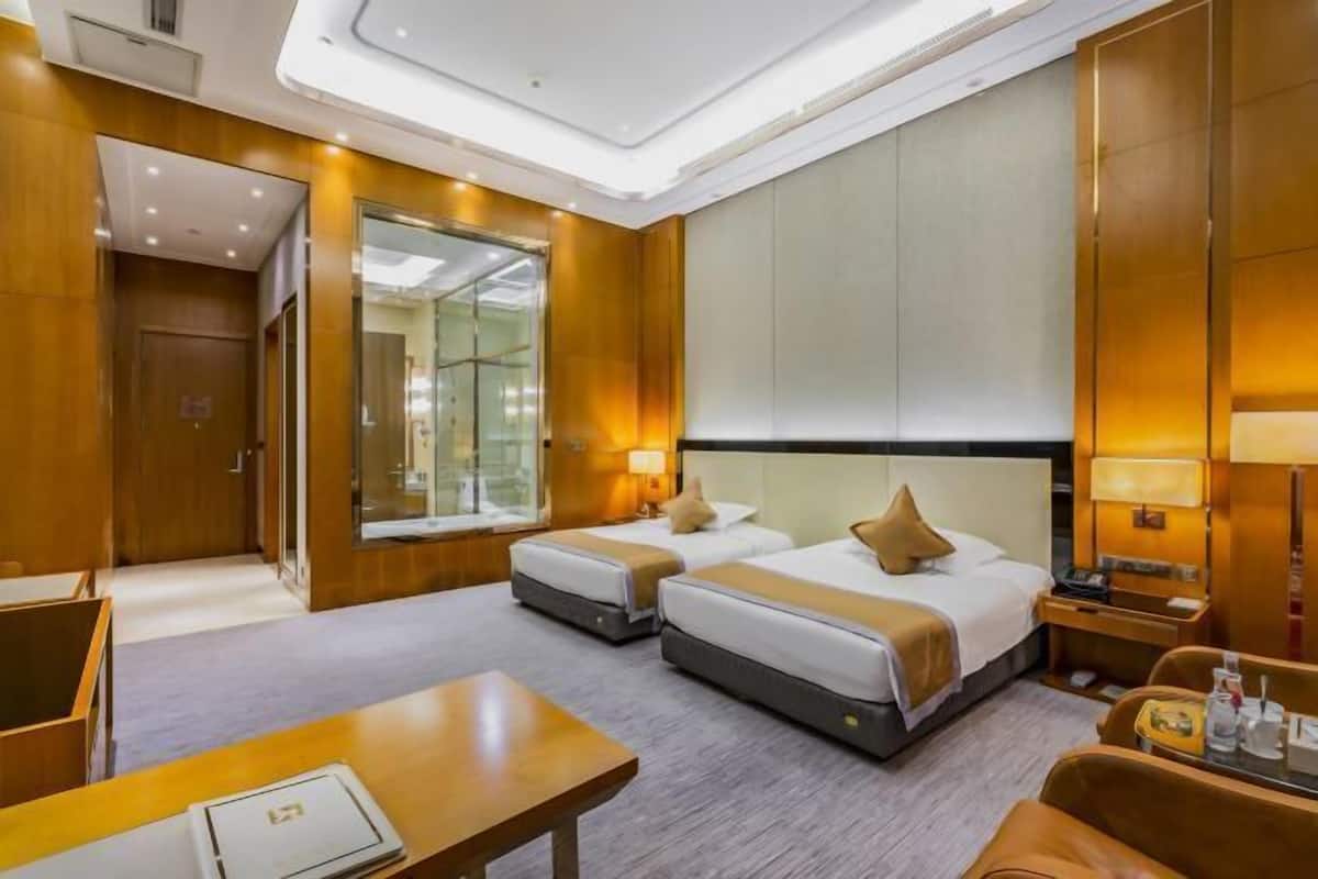 Habitación de hotel con dos camas, un escritorio, una silla, un espejo y la puerta del baño.
