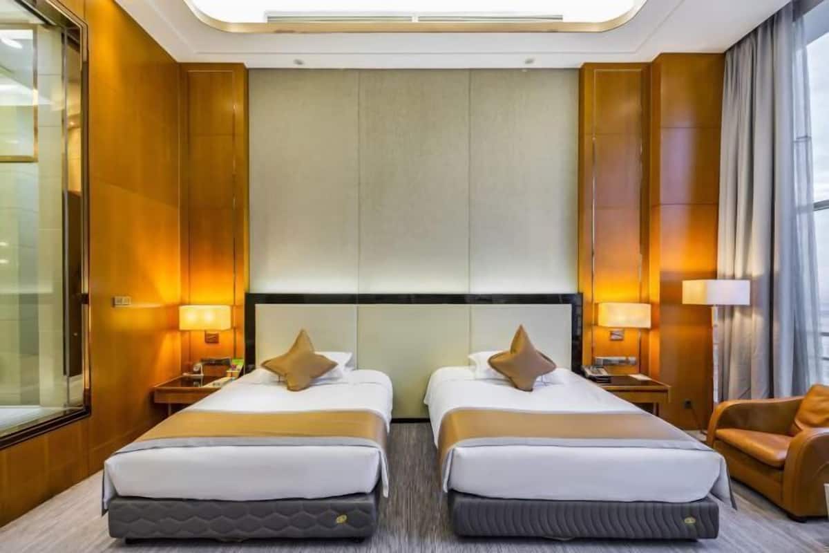 Habitación de hotel con dos camas, un sofá y un ventanal grande.