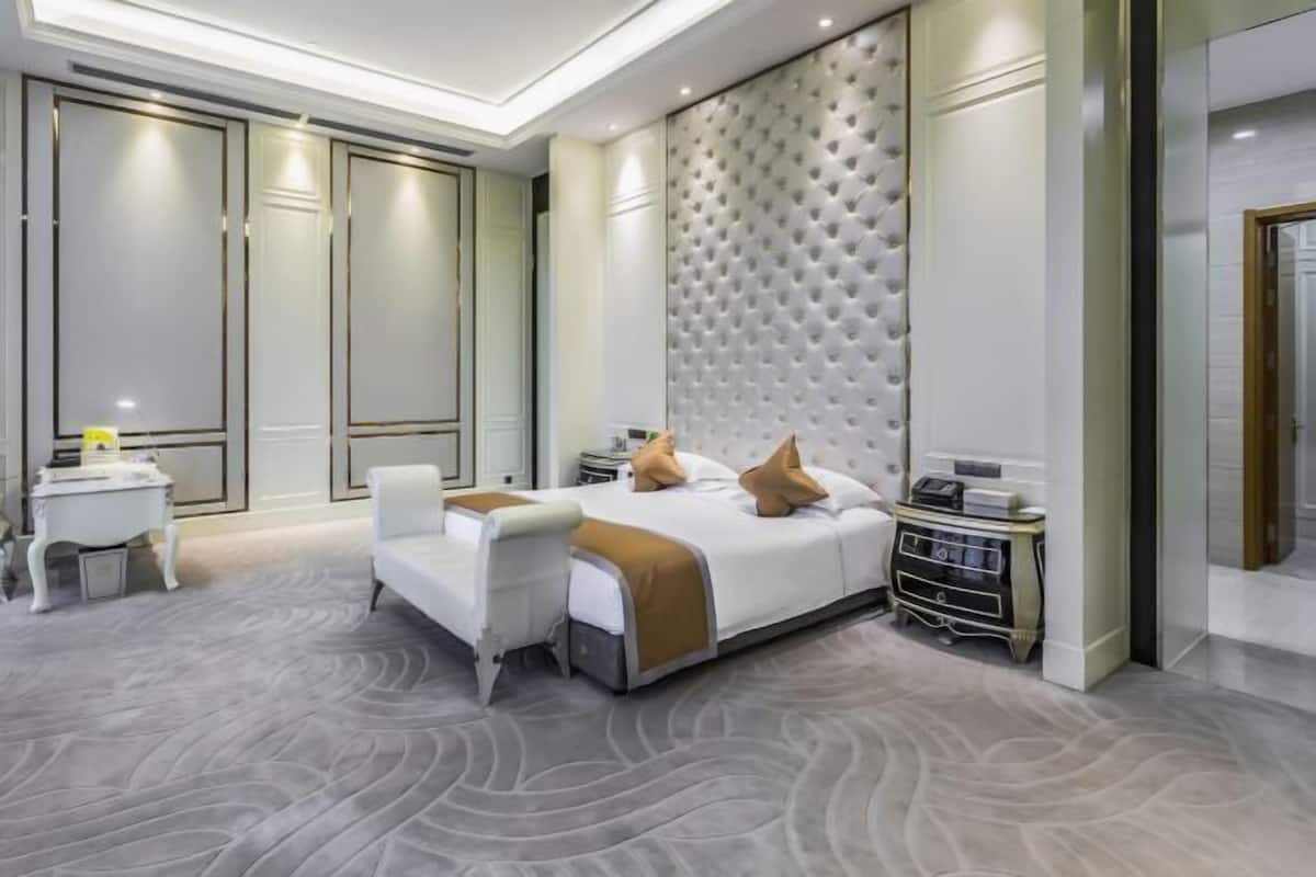 Una habitación de hotel moderna con una cama grande, un sillón blanco, una mesita de noche y un televisor montado en la pared.