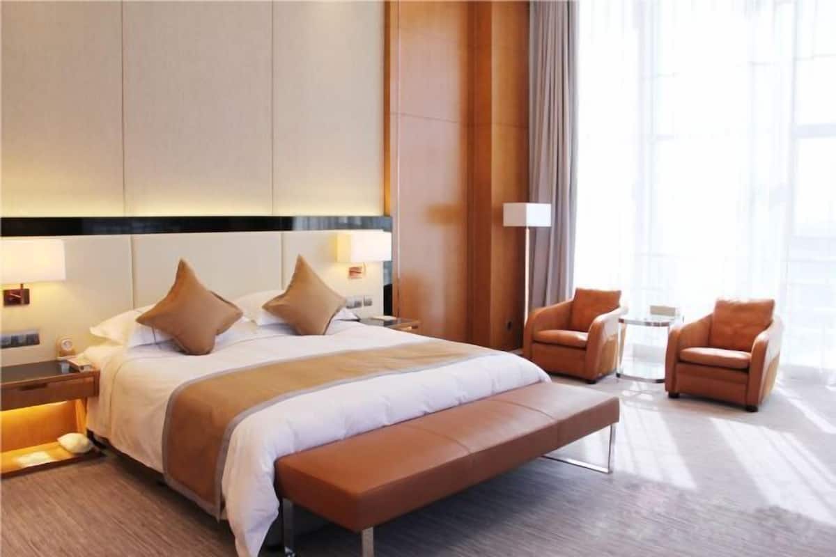 Una habitación de hotel moderna con una cama grande, un banco, dos sillones y una mesita de noche.