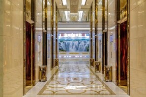 A corridor with a patterned floor, glass doors, and a waterfall mural at the end. - Jiujiang Hotel (Qian'an)