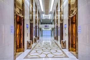A hotel corridor with elevators, a patterned floor, and directional signs.