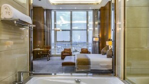 A modern hotel room with a large window, a bathtub, and a seating area with chairs and a table. - Jiujiang Hotel (Qian'an)