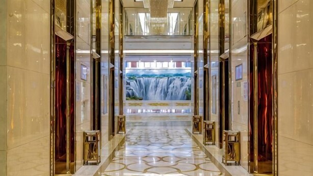 A corridor with a waterfall mural, polished marble floors, and gold accents. - Jiujiang Hotel (Qian'an)