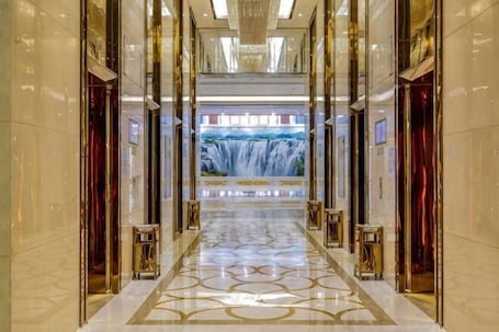 A corridor with a waterfall mural, polished marble floors, and gold accents.. Jiujiang Hotel