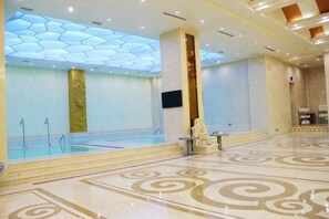 A spacious indoor swimming pool area with a modern ceiling design, a seating area, and a patterned floor. - Jiujiang Hotel (Qian'an)