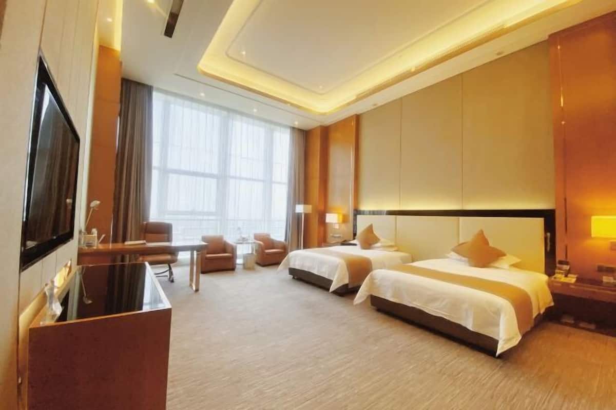 Habitación de hotel con dos camas, un escritorio, una silla, un televisor y un ventanal grande.