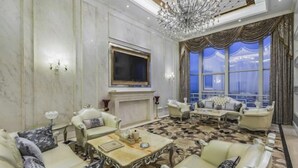 A luxurious living room with a fireplace, elegant furniture, a large TV, and a chandelier.
