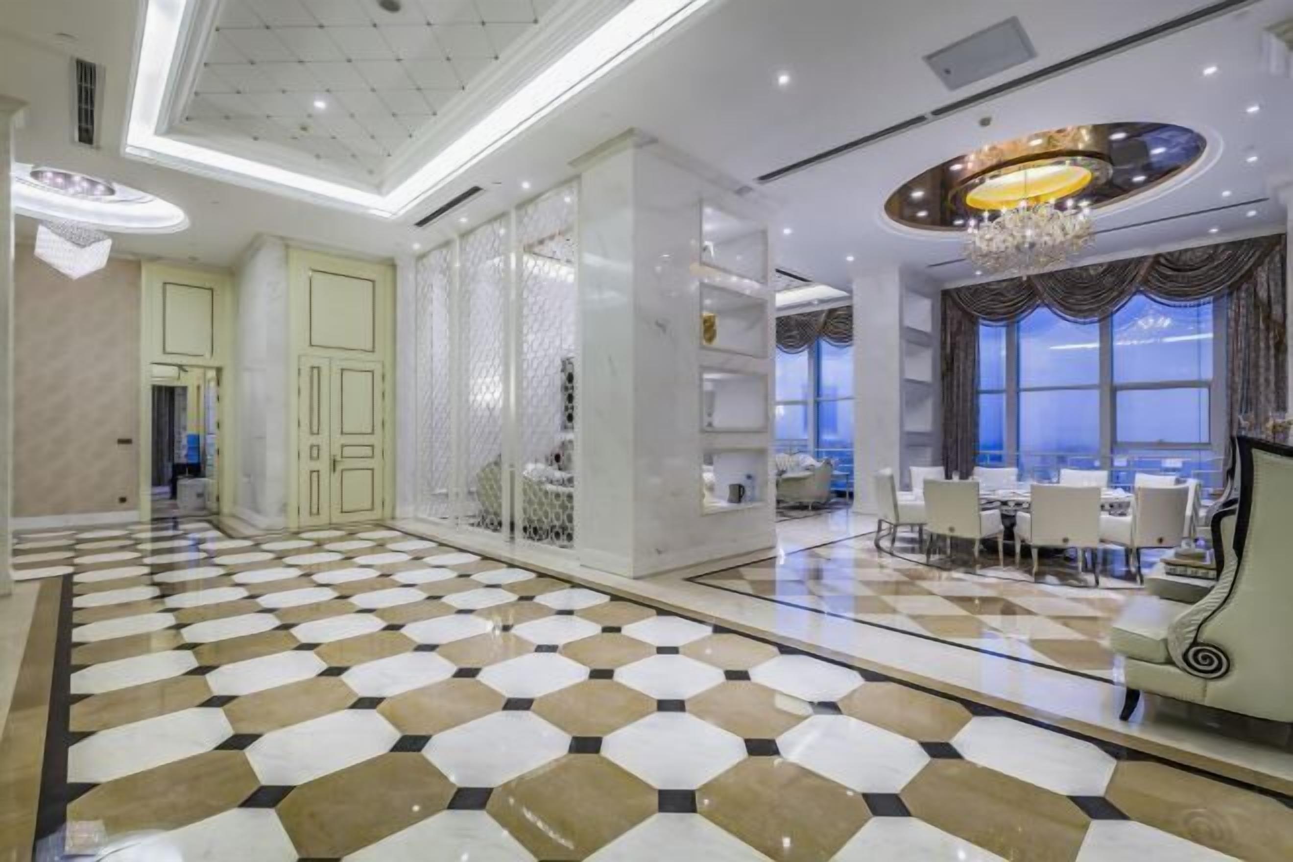 Un hall d’hôtel avec un sol à carreaux, un lustre et un espace repas comprenant des tables et des chaises.