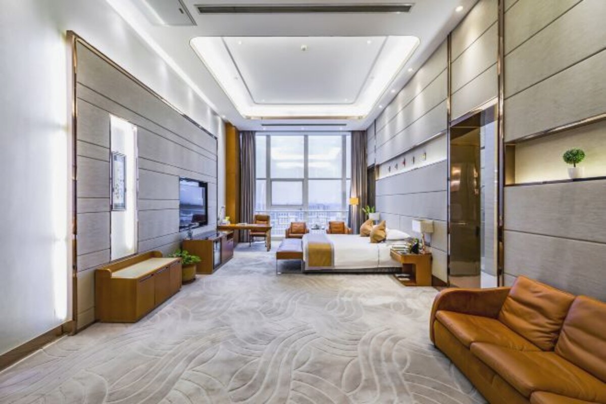 A modern hotel room with a large bed, a sofa, a TV, and a view of the city.
