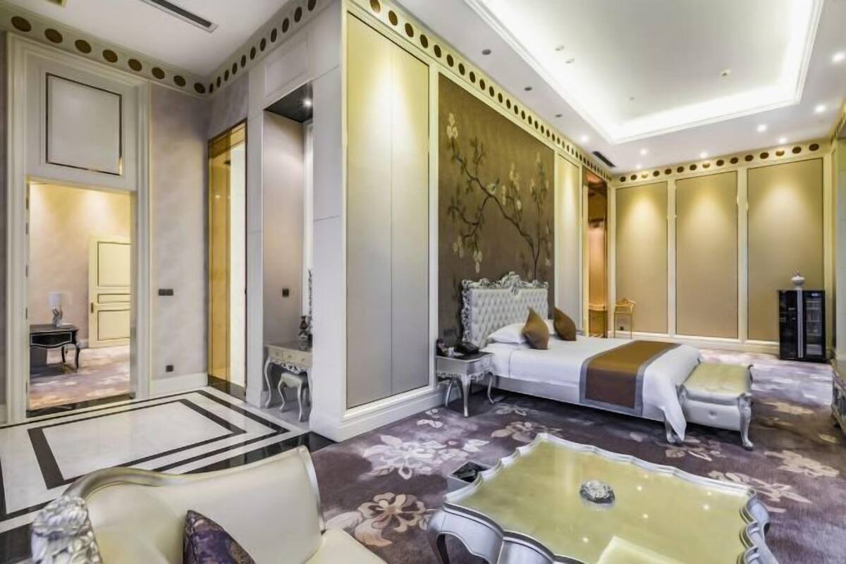 Habitación de hotel con una cama grande, un rincón de descanso con una mesa y un detalle decorativo en la pared.