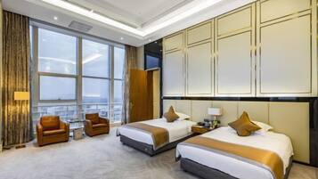 Une chambre d’hôtel avec deux lits, un coin salon comprenant un canapé et des fauteuils, une grande fenêtre et un mini-bar.