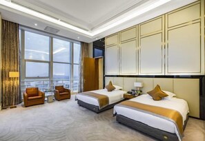 A hotel room with two beds, a sitting area with a sofa and armchairs, a large window, and a minibar. - Jiujiang Hotel (Qian'an)