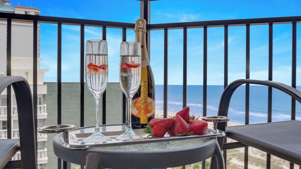 Un balcon avec deux flûtes à champagne, une bouteille et des fraises disposées sur un plateau.