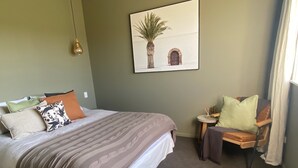 Et hotelværelse med en seng, en stol, et lille bord med en plante og et billed på væggen.